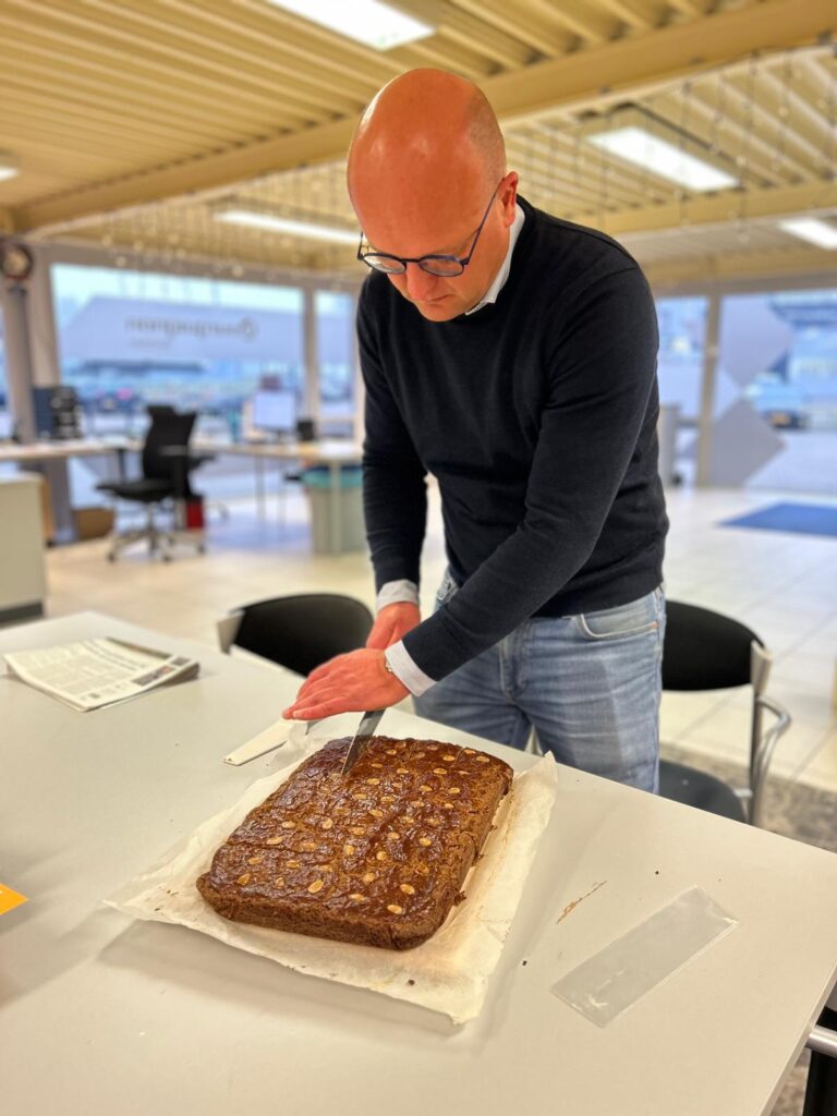 Collega Erwin snijdt zelfgemaakte speculaas aan op kantoor Bourguignon Lease